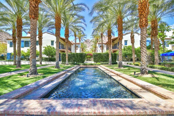 A rectangular pool with a brick border, surrounded by palm trees and a well-maintained lawn. - La Quinta En-Suite Studio, Private Patio, Fireplace, Views, Gym, Pools (La Quinta)