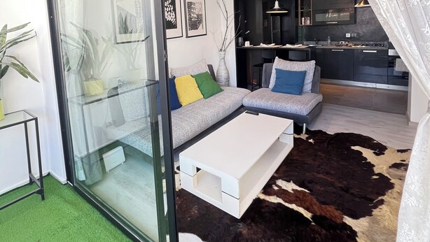 A modern living room with a glass sliding door, a sofa with colorful cushions, a white coffee table, and a cowhide rug. - Stay in GAUTHIER studio M (Casablanca)