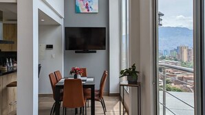 A modern dining area with a large window, a flat-screen TV, and a colorful abstract painting on the wall. - Exclusive Luxury In Heart of Medellin. (Medellín)