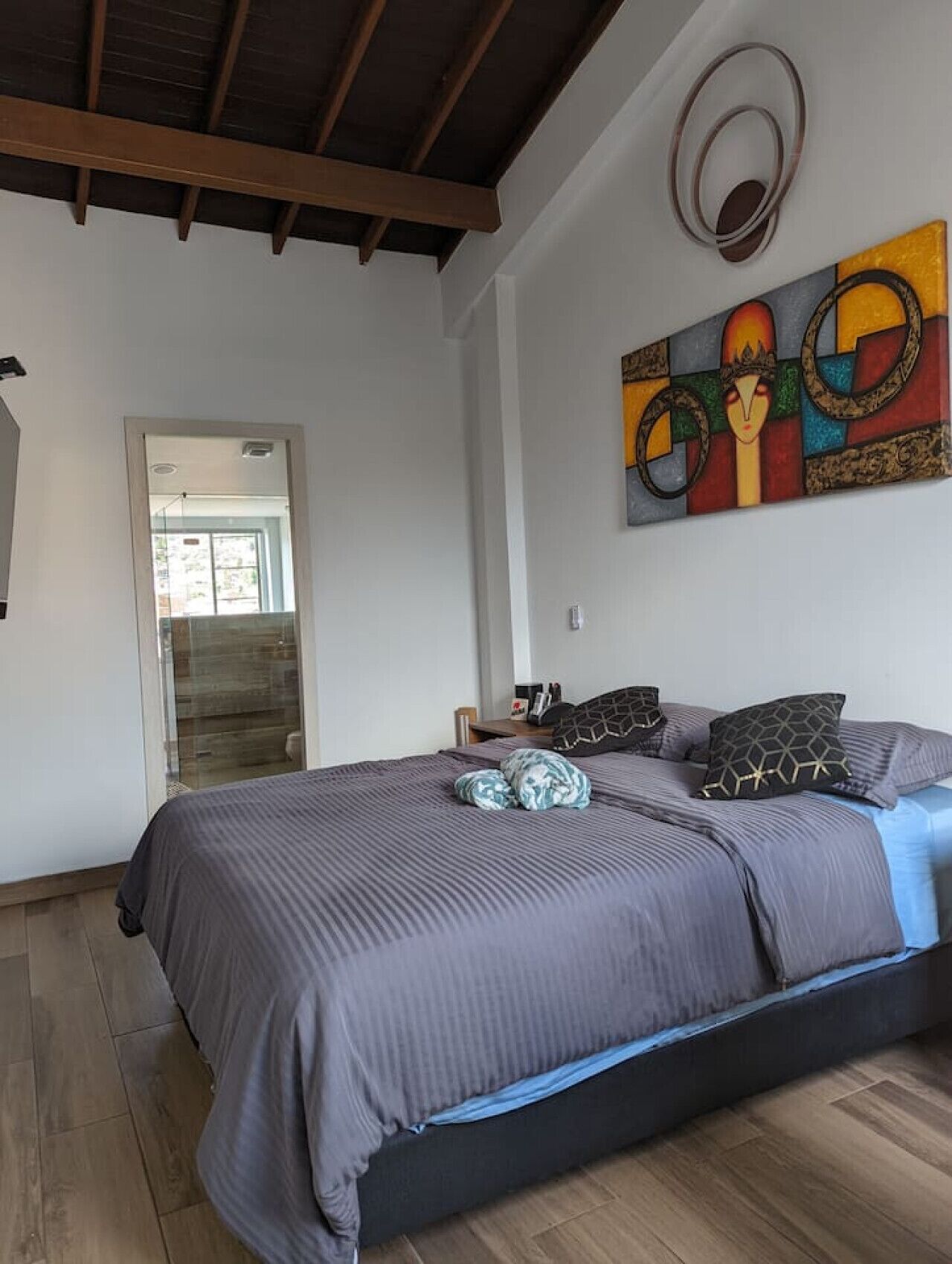 A bedroom with a bed, pillows, a painting, and a wooden floor.