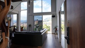 A spacious living area with a large window offering a city view, a dark-colored sofa, and a wooden ceiling structure. - Exclusive Luxury In Heart of Medellin. (Medellín)