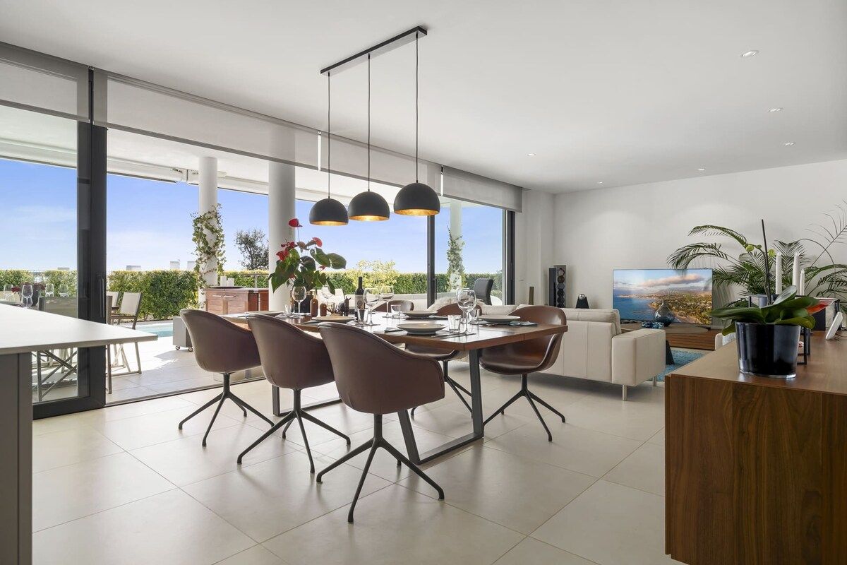 Een moderne eetruimte met een grote tafel, stoelen, hanglampen en uitzicht op de omgeving.