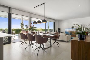 A modern dining area with a large table, chairs, pendant lights, and a view of the outdoors.
