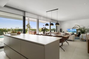 Et moderne interiør med en køkkenø, spiseplads og udsigt til det fri.