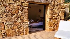 Habitación con paredes de piedra, una cama y una terraza de madera.
