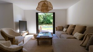 Una sala de estar con sofá, sillones, una mesa de centro y televisor. Hay un ventanal con vistas a zonas verdes.