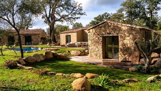 Una casa de piedra con piscina, rodeada de un césped cuidado y grandes rocas.