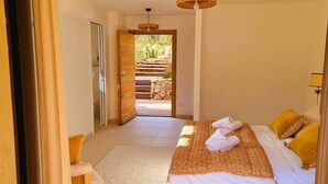 Una habitación de hotel con una cama, una puerta de madera que da a un balcón y vistas de una escalera de piedra.