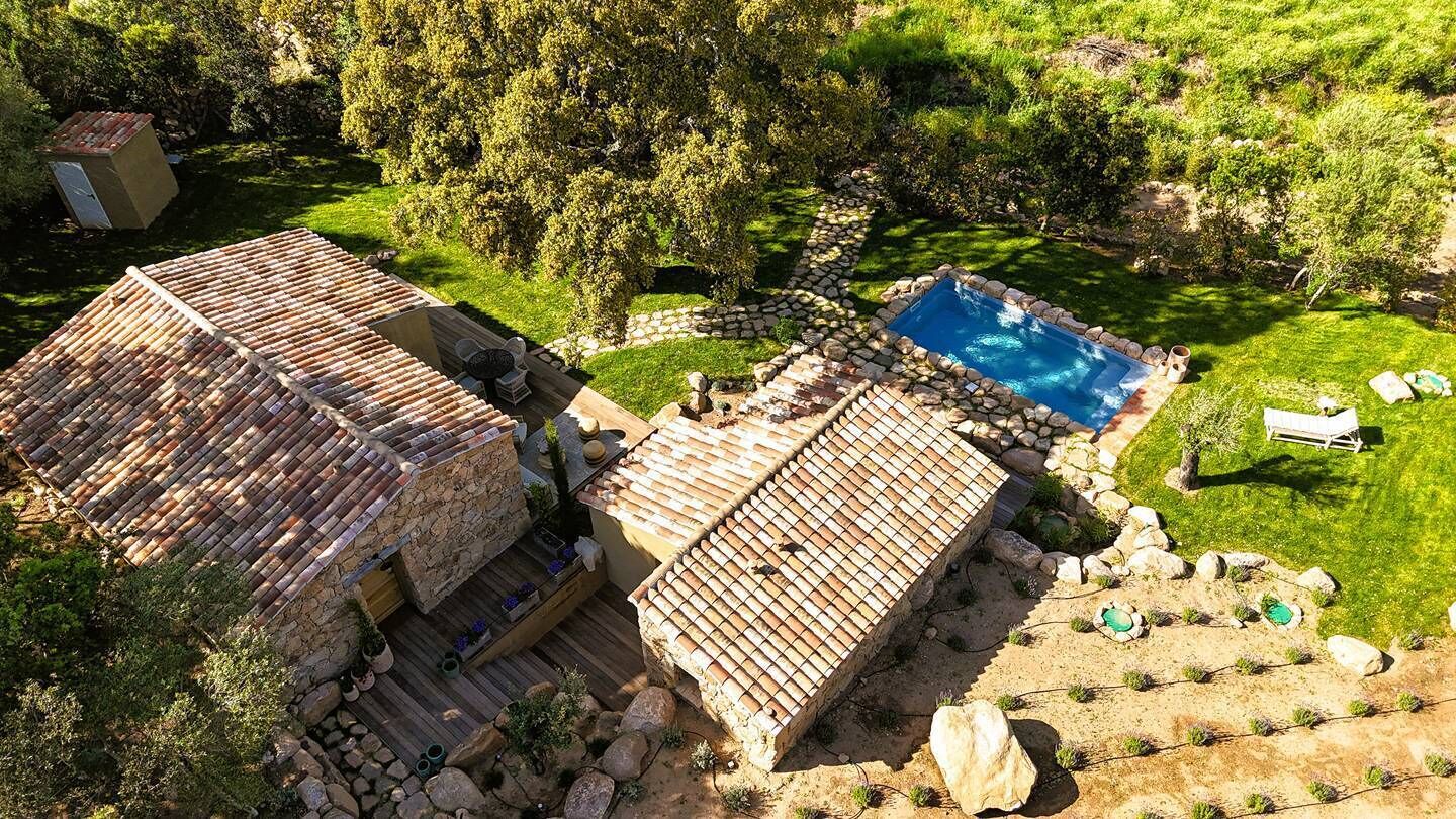 A rustic villa with a stone facade, a tiled roof, and a swimming pool surrounded by a stone border.