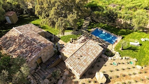 Une villa de style rustique, avec une façade en pierre, un toit en tuiles et une piscine entourée d’une bordure en pierre.