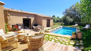 A pool area with a stone patio, wicker furniture, and a small garden with a lawn and trees.