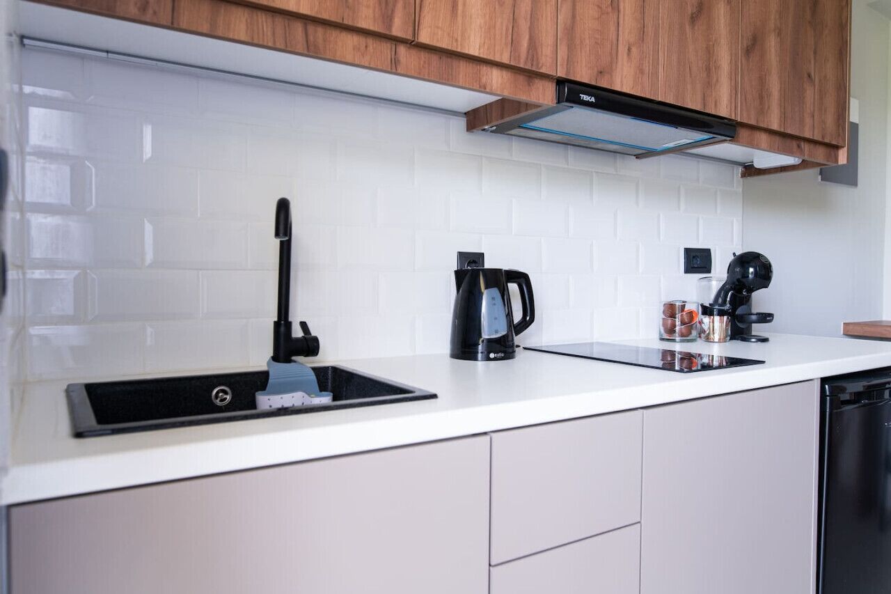Una cocina moderna con armarios blancos, un grifo negro, una cafetera y un tostador.