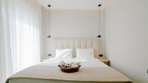 A neatly made bed with a white headboard, a bedside table with a lamp, and a basket of toiletries on the bed. - Aelia Prime Experience 2 (Kos)