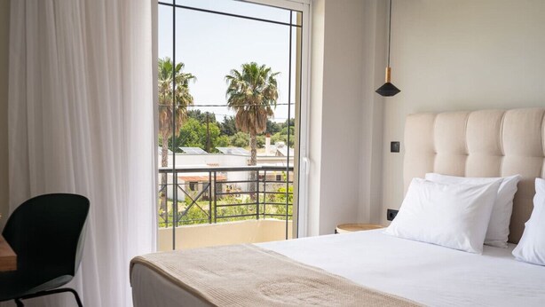A hotel room with a large bed, a view of palm trees and a balcony. - Aelia Prime Experience 2 (Kos)