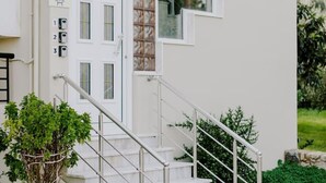 A modern building with a white exterior, a staircase with metal railings, and a potted plant at the base. - Aelia Prime Experience 2 (Kos)