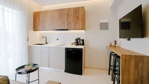 A modern kitchen with wooden cabinets, a black dishwasher, and a built-in TV. - Aelia Prime Experience 2 (Kos)