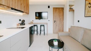 A modern kitchen with a central island, bar stools, a flat-screen TV, and a sofa in a living area. - Aelia Prime Experience 2 (Kos)