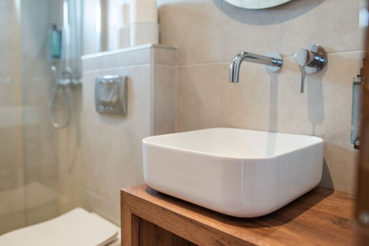 A bathroom with a white sink, a wooden vanity, and a shower area.
