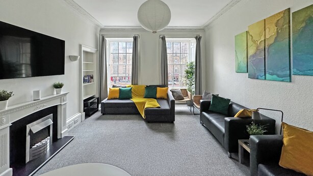 A living room with a fireplace, a large flat-screen TV, a sofa set, and a painting on the wall.