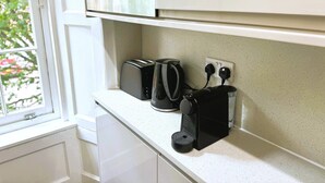 A kitchen with white cabinets, a toaster, a coffee maker, and a kettle on the countertop.