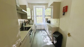 A narrow kitchen with a window, a washing machine, and a fire blanket on the wall.