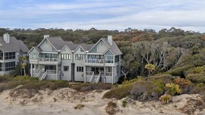 A large, multi-story beachfront house with multiple balconies and a staircase leading to the upper levels.