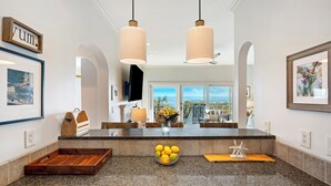 A kitchen with granite countertops, a wooden fruit bowl, and hanging pendant lights.
