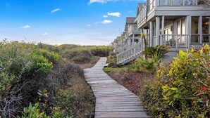 A wooden boardwalk leading to a beachfront property with multiple balconies and large windows.