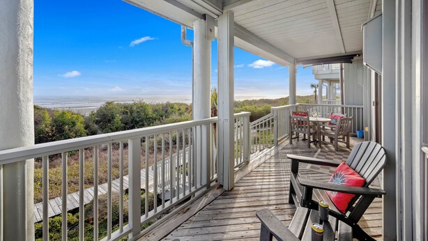 A wooden deck with a railing, overlooking a beach and ocean.