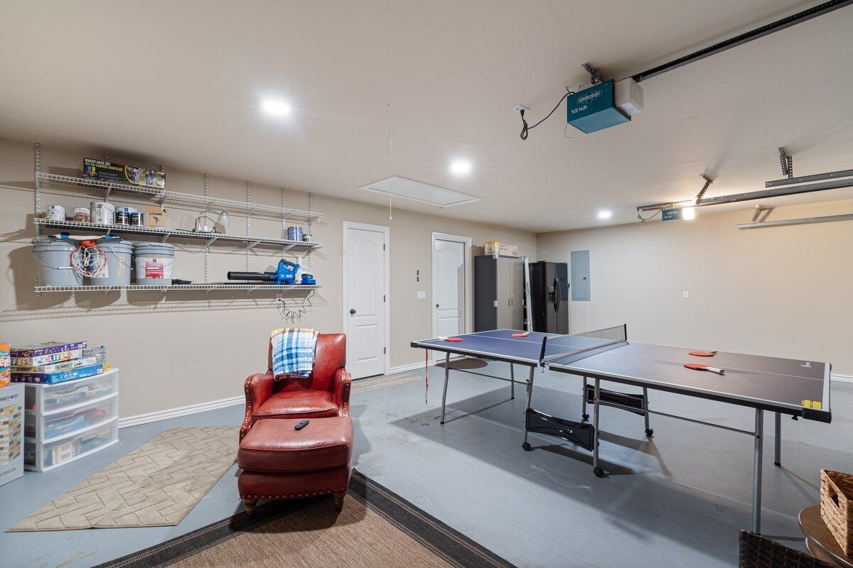 Et værelse med et ping pong-bord, en læderstol i rød farve, hylder med opbevaringskasser og en projektor monteret i loftet.