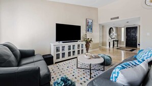 Un salon moderne avec un téléviseur à écran plat, un meuble blanc, une table basse ronde et deux canapés.
