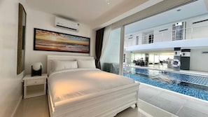 A hotel room with a large bed, a painting, an air conditioning unit, and a view of a pool and upper-level balcony. - B12 - 2 Bedroom Condo With Pool Access, Karon Beach (Karon)