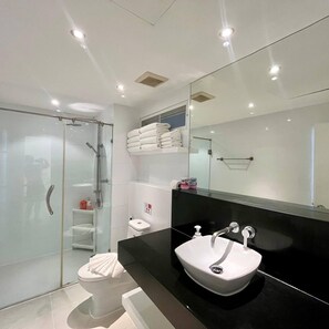 A modern bathroom with a glass shower enclosure, a white toilet, a black countertop with a white sink, and a large mirror. - B12 - 2 Bedroom Condo With Pool Access, Karon Beach (Karon)