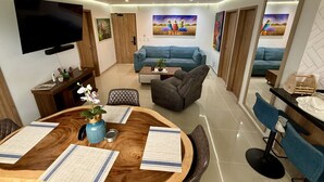 Ein modernes Wohnzimmer mit einem Holzespeisetisch, blauen Sofas und einem an der Wand befestigten Flachbildfernseher.