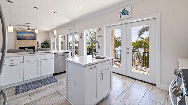 Una cocina moderna con armarios blancos, una isla central y vistas al exterior a través de grandes puertas correderas.