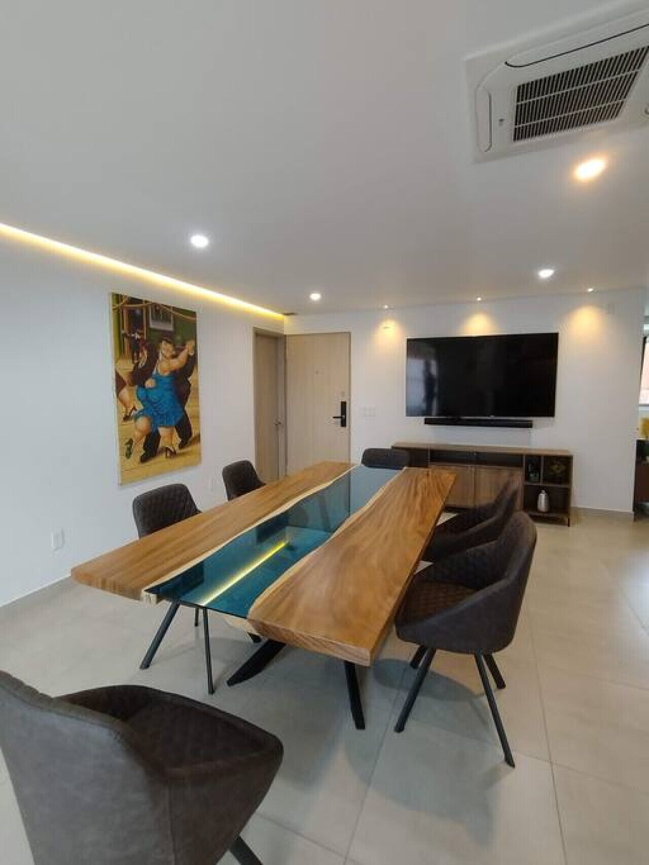 Une salle de conférence moderne, dotée d’une longue table, de chaises, d’un grand téléviseur et d’un tableau accroché au mur.