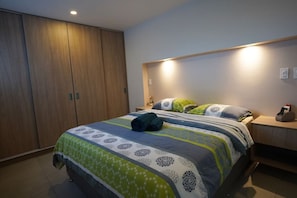 A bedroom with a bed, a wardrobe, a bedside table with a phone, and a wall-mounted light.