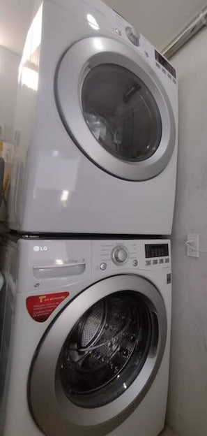 A stacked washer and dryer unit with control panels and a red warning label.