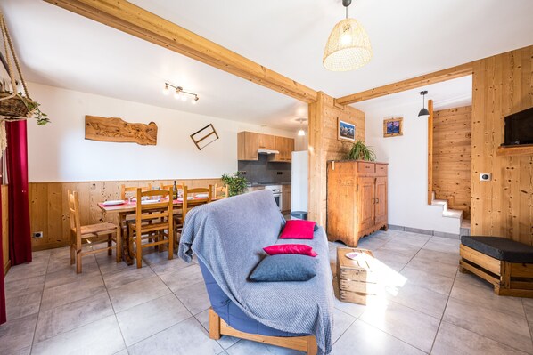 Un vaste espace de vie comprenant un canapé, une table à manger en bois et des chaises. On aperçoit une cuisine au fond.