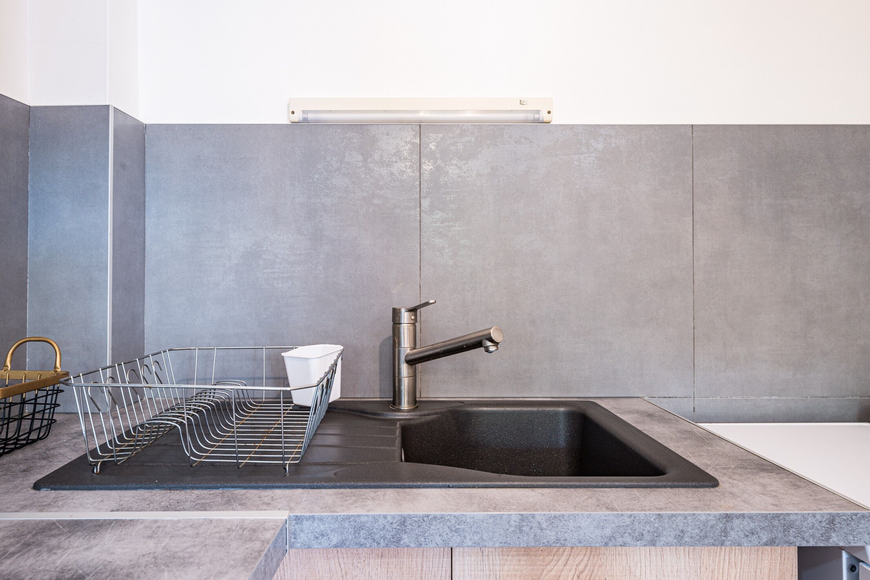 A kitchen with a stainless steel sink, a wire basket, and a light fixture above the counter.