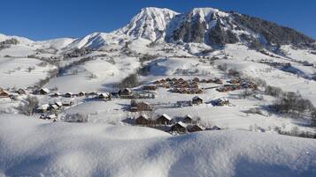 Une montagne enneigée sous un ciel dégagé, un village aux maisons en bois et un sommet imposant.