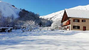 A snow-covered village with a wooden building featuring balconies and a snow-covered mountain in the background.