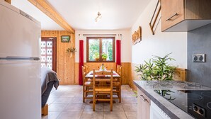 A compact kitchen with wooden cabinetry, a dining table, chairs, a built-in stove, and a window with curtains.