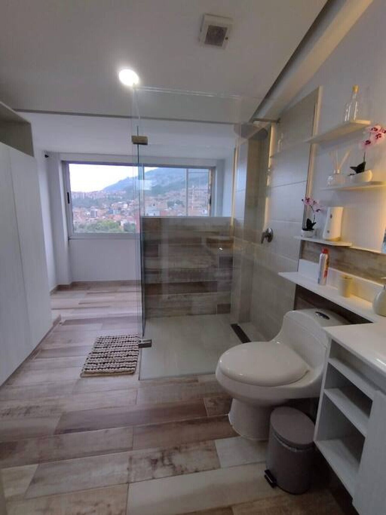 Un baño moderno con cabina de ducha de vidrio, un inodoro y un pequeño cubo de basura.