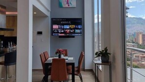 Un comedor moderno con un gran ventanal, un televisor de pantalla plana en la pared y una alfombra colorida en el suelo.