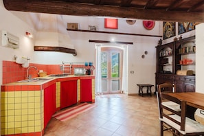 Une cuisine avec des carreaux rouges et jaunes, une table à manger en bois et une vue à travers une porte vitrée.