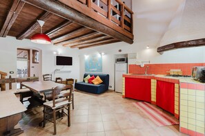 A kitchen with a red countertop, a dining area with wooden furniture, a blue sofa, and a wooden ceiling structure. - Villa Loft 'Antico Baglio' – Scopello – Mountain View, Wi-Fi, Air Conditioning (Castellammare del Golfo)