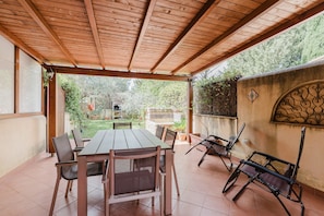 Une terrasse extérieure avec une table et des chaises en bois, une pergola au-dessus et une vue sur un jardin.