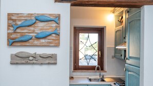 A kitchen with teal cabinets, a wooden fish decoration, and a window with a star-shaped design. - Apartment 'Casa Lauretta' with Sea View, Shared Pool and Air Conditioning (Porto Pollo)