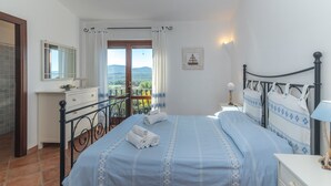 A bedroom with a bed, a bedside table, a nightstand, a window with curtains, a view of the outdoors, and a small framed picture on the wall. - Apartment 'Casa Lauretta' with Sea View, Shared Pool and Air Conditioning (Porto Pollo)